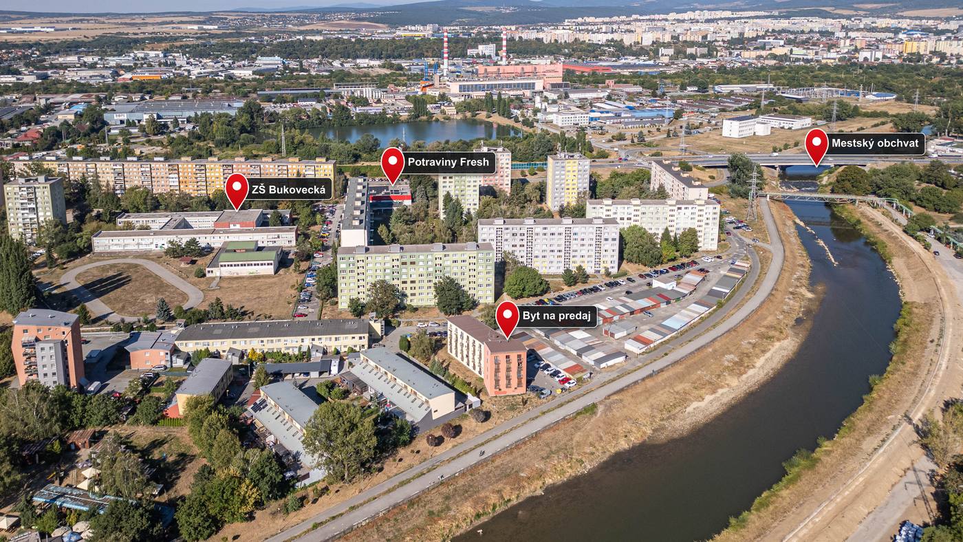 Letecký záber sídliska so zakreslenými pinmi — byt na predaj, základná škola, potraviny a mestský obchvat